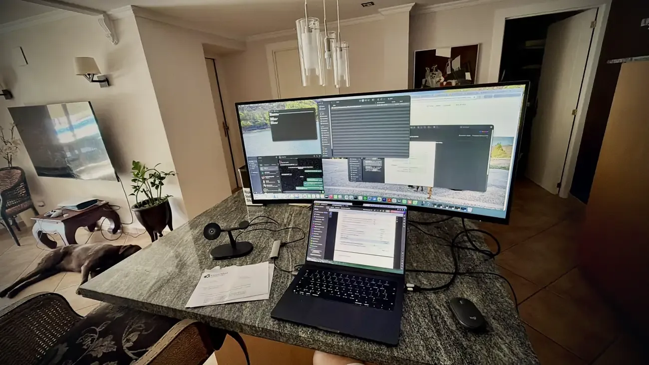 De nieuwe brede monitor naast de laptop op de granieten tafel, met Mo op de achtergrond