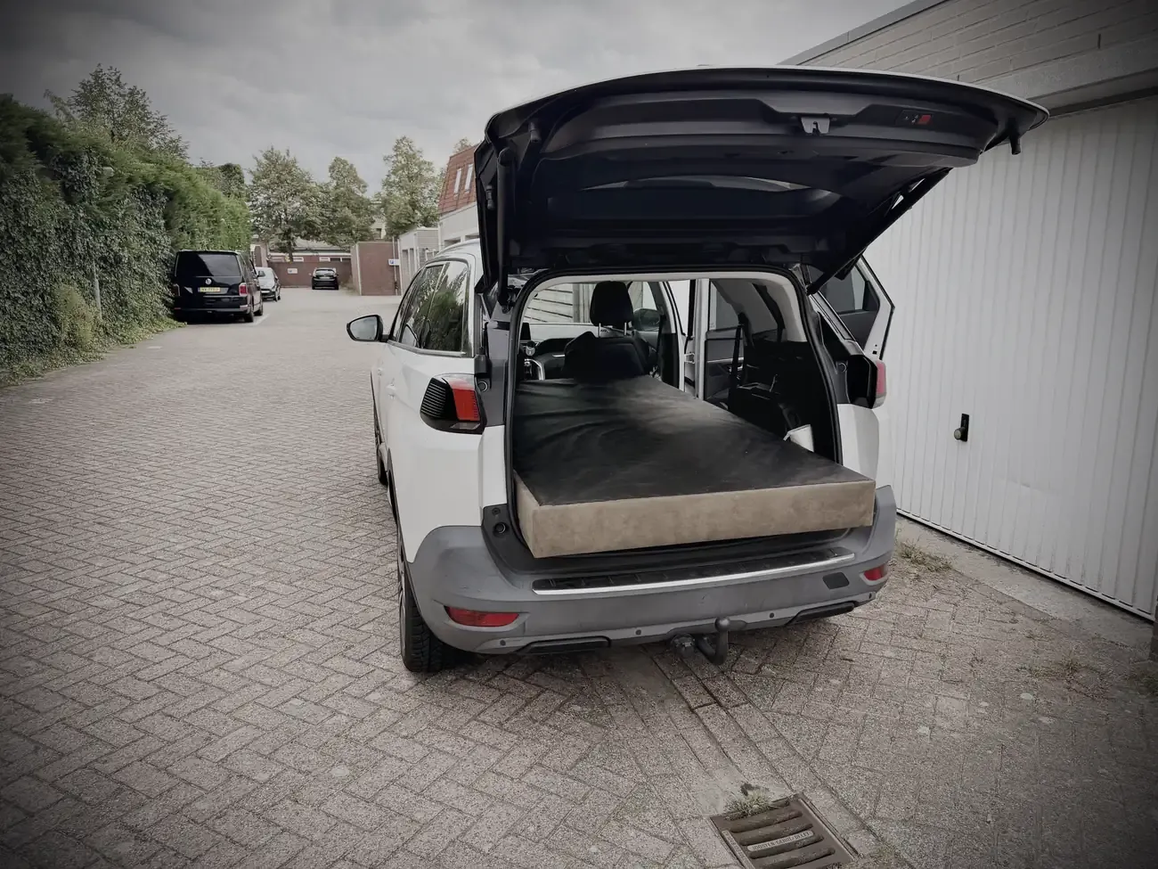 De achterbak open met een matras erin, op de oprit in Hoeven