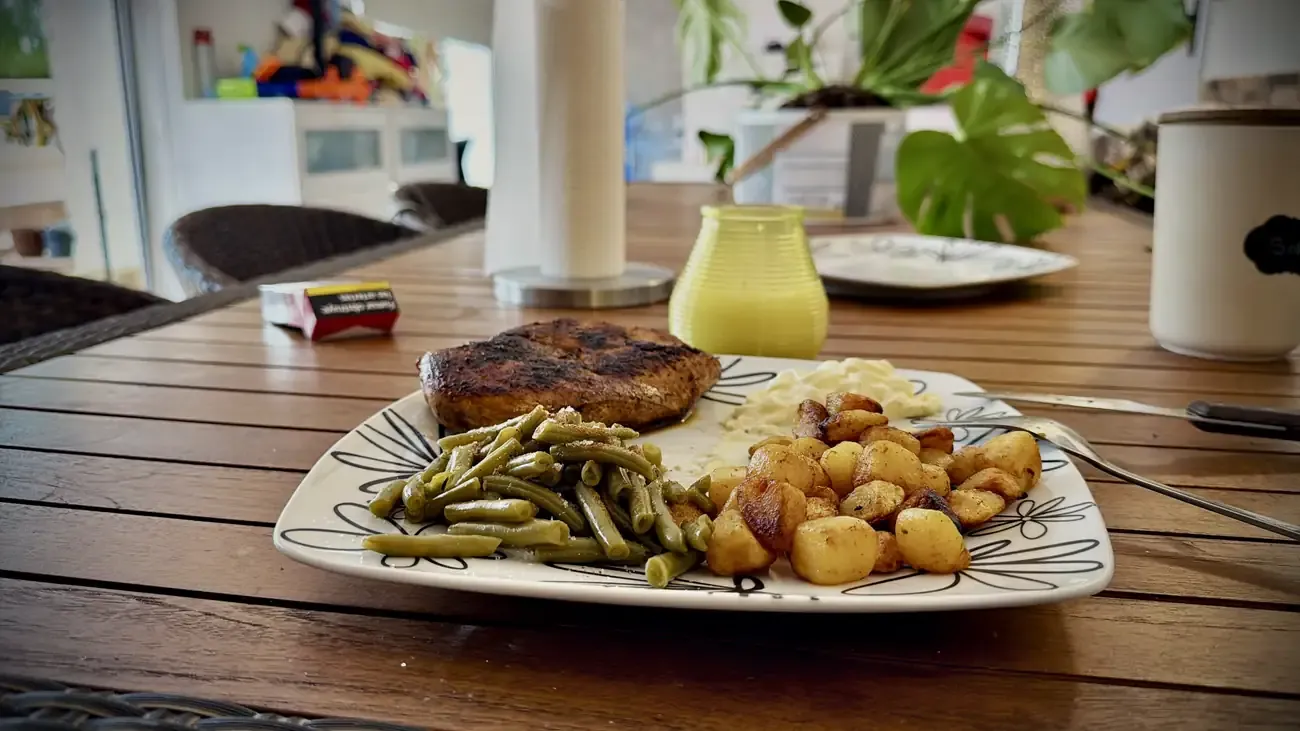 Een bord met gebakken aardappelen, sperziebonen en kipfilet