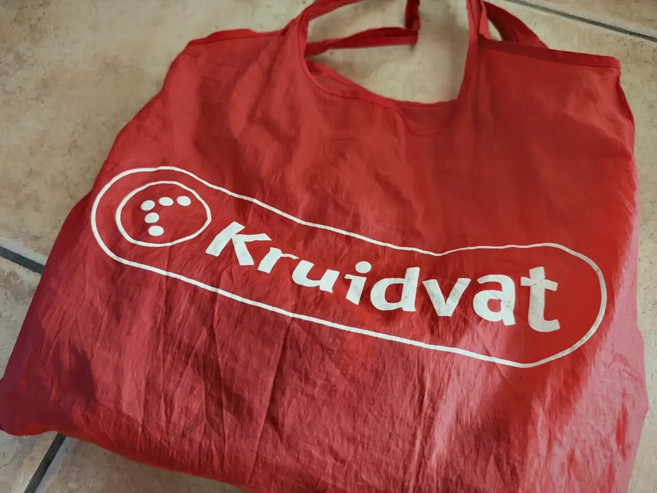 Het rode Kruidvat-tasje waar mijn water in zat, op de tegels