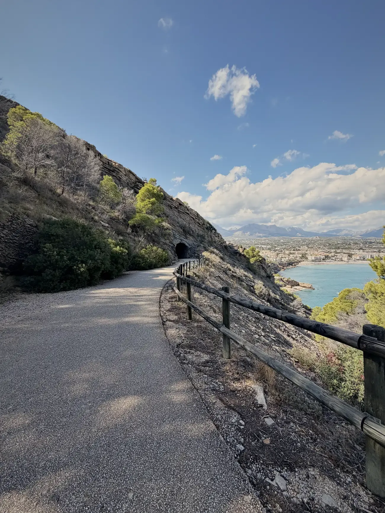 Het brede wandelpad langs de rotsen, met een hek langs de rand en een tunnel verderop