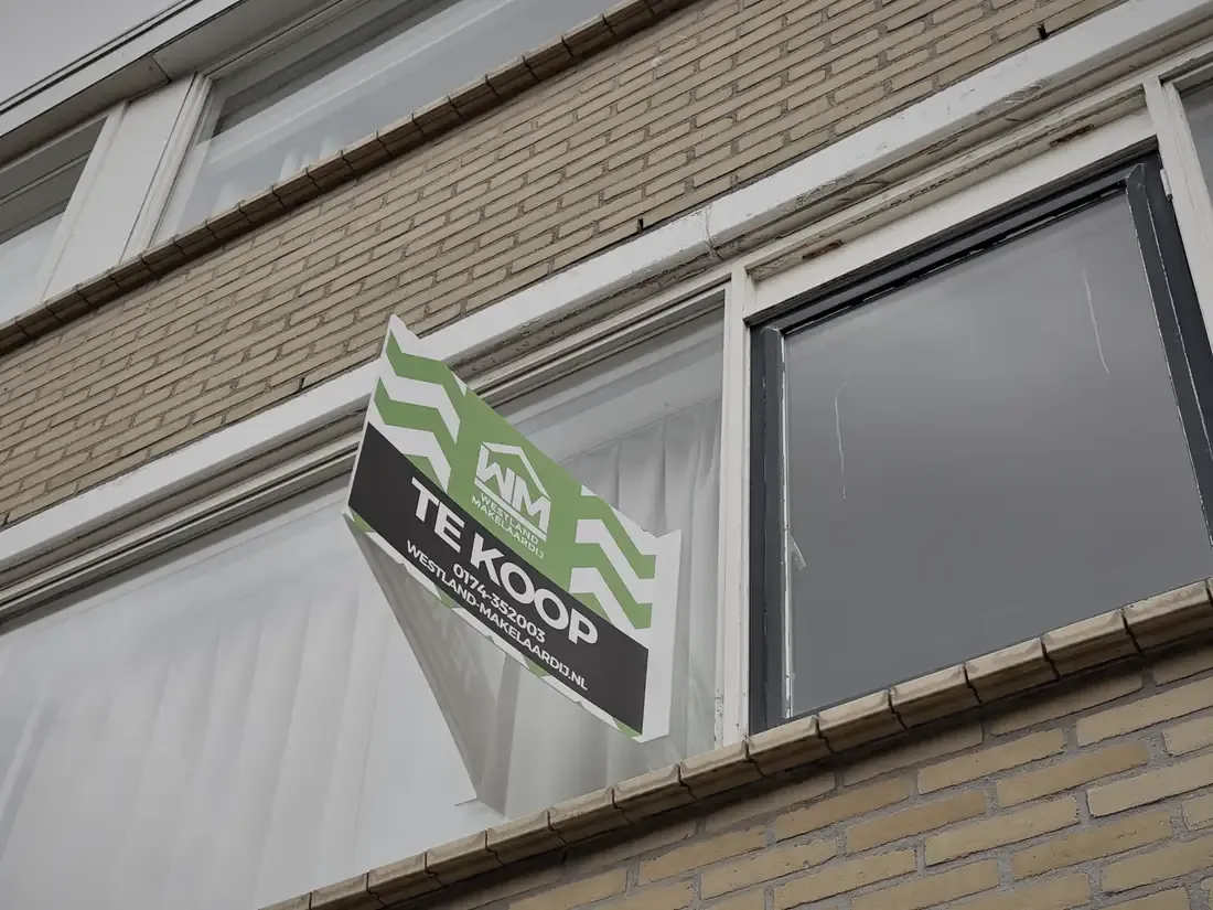 Het te-koop-bord van de makelaar aan de gevel
