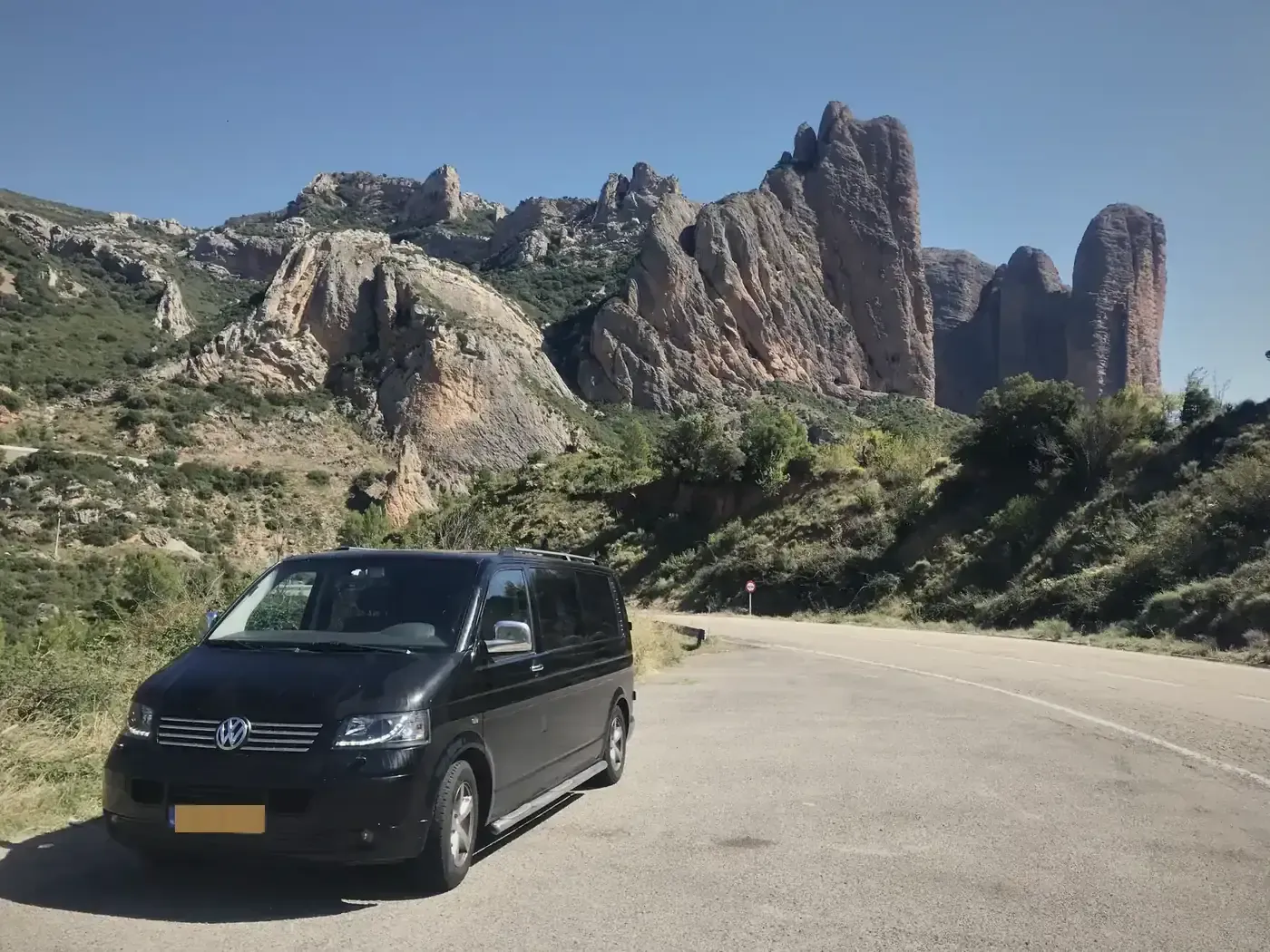 De zwarte Transporter op een bergweg in de Pyreneeën, met de rotsen van de Mallos erachter